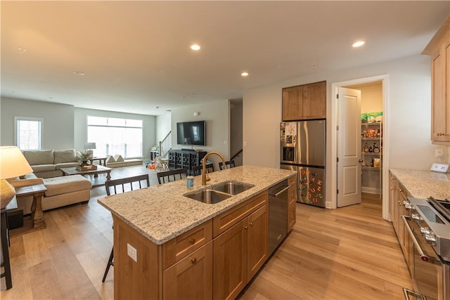 kitchen with stainless steel appliances, a kitchen island with sink, sink, and light hardwood / wood-style flooring