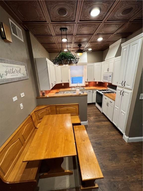 kitchen featuring sink, white appliances, white cabinetry, dark hardwood / wood-style flooring, and kitchen peninsula