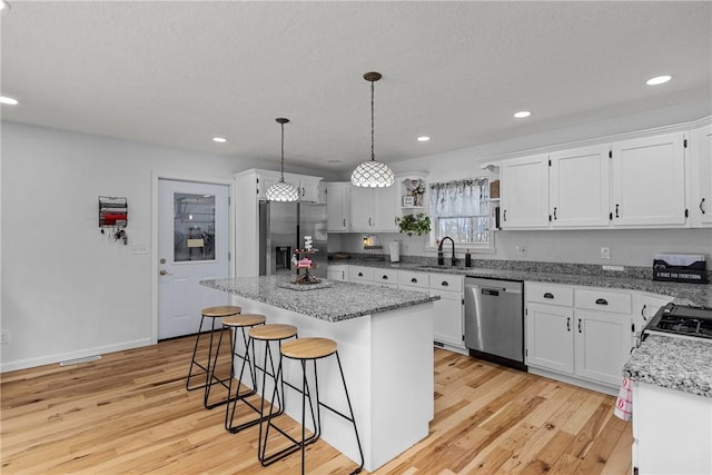 kitchen featuring pendant lighting, sink, appliances with stainless steel finishes, white cabinetry, and a kitchen island