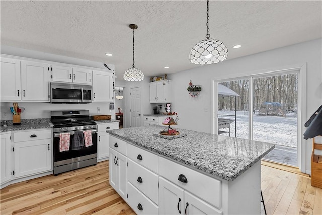 kitchen with white cabinetry, appliances with stainless steel finishes, a center island, and decorative light fixtures