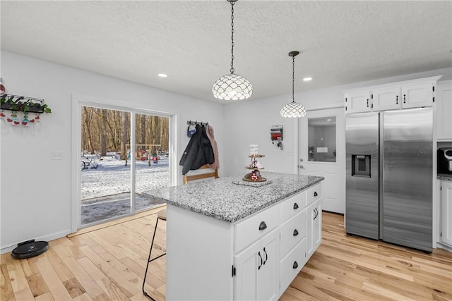 kitchen with stainless steel fridge, white cabinets, a kitchen island, decorative light fixtures, and light wood-type flooring