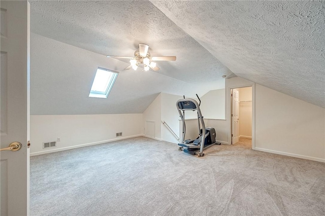 additional living space featuring a textured ceiling, lofted ceiling with skylight, light colored carpet, and ceiling fan