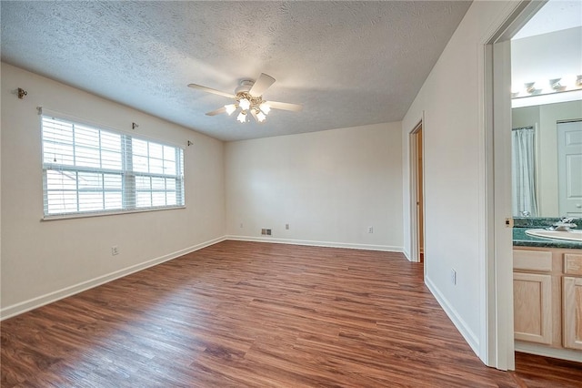 interior space with ensuite bathroom, sink, ceiling fan, dark wood-type flooring, and a textured ceiling