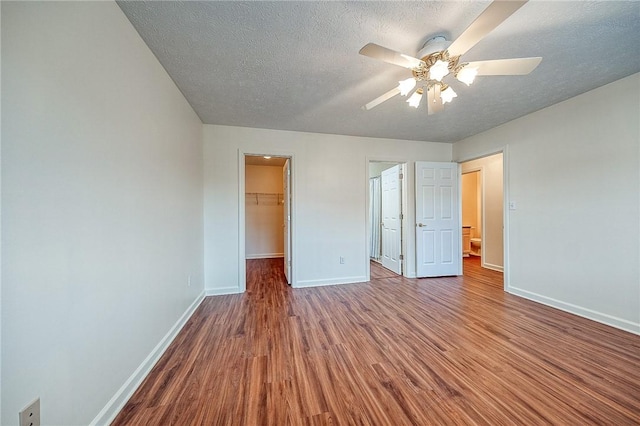 unfurnished bedroom with hardwood / wood-style flooring, a walk in closet, ceiling fan, a textured ceiling, and a closet