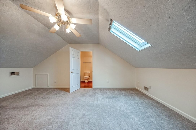 additional living space with ceiling fan, a textured ceiling, light colored carpet, and vaulted ceiling with skylight