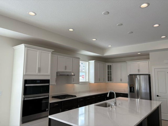 kitchen featuring sink, white cabinetry, stainless steel appliances, an island with sink, and a textured ceiling