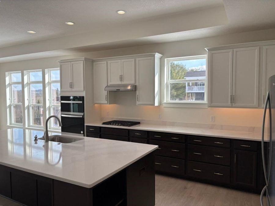 kitchen with sink, white cabinetry, light hardwood / wood-style flooring, an island with sink, and black appliances