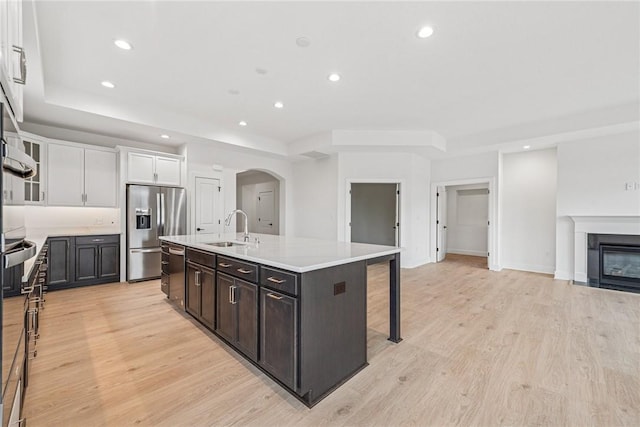 kitchen with light wood-type flooring, a fireplace with flush hearth, a sink, stainless steel appliances, and arched walkways