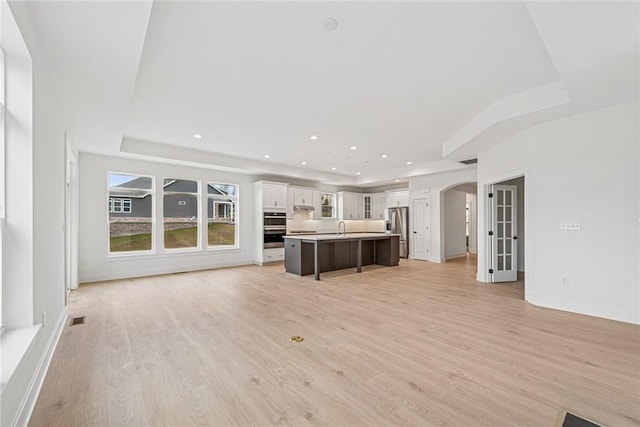 unfurnished living room featuring visible vents, light wood-style flooring, recessed lighting, arched walkways, and a sink