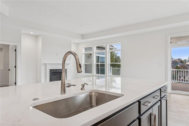 kitchen featuring a sink, light stone counters, a glass covered fireplace, recessed lighting, and light wood-style floors