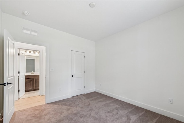 unfurnished bedroom with visible vents, connected bathroom, baseboards, light colored carpet, and a sink