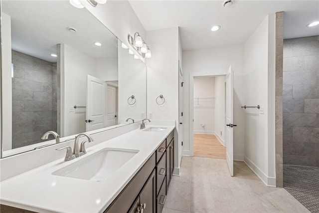 bathroom with double vanity, walk in shower, baseboards, and a sink