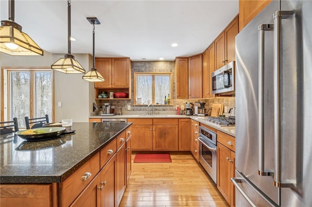 kitchen featuring sink, hanging light fixtures, appliances with stainless steel finishes, a kitchen island, and dark stone counters