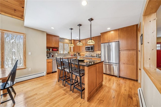 kitchen featuring a kitchen island, appliances with stainless steel finishes, hanging light fixtures, baseboard heating, and light hardwood / wood-style flooring