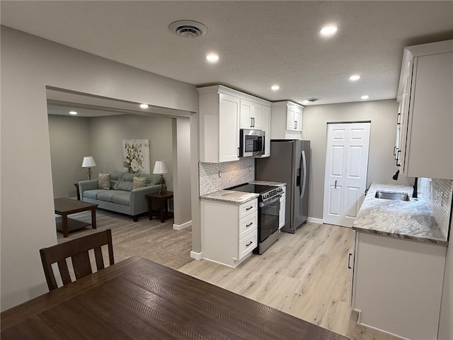 kitchen featuring appliances with stainless steel finishes, white cabinets, decorative backsplash, light stone counters, and light wood-type flooring