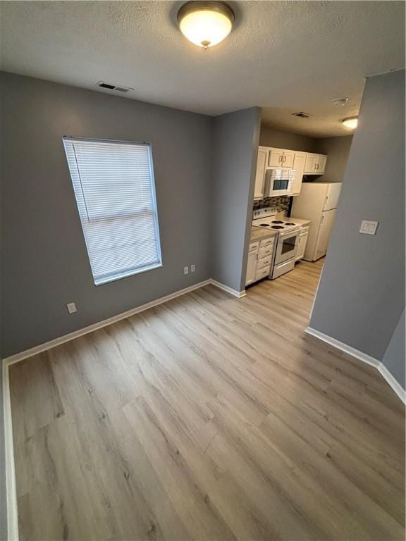 kitchen featuring white appliances, light hardwood / wood-style flooring, a textured ceiling, and white cabinets