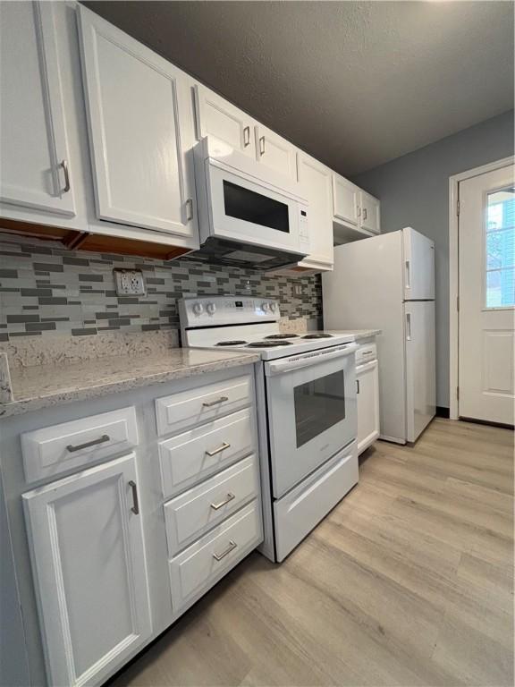 kitchen featuring tasteful backsplash, light stone counters, white appliances, light hardwood / wood-style floors, and white cabinets