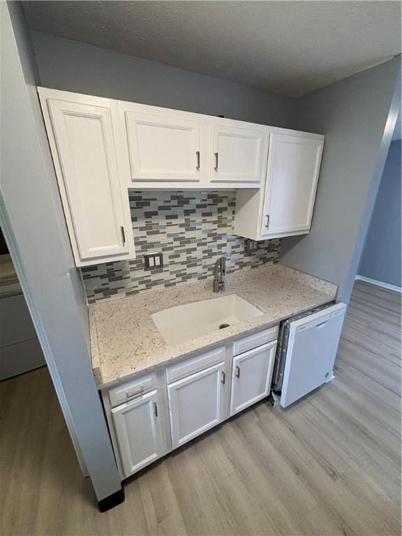 kitchen with white dishwasher, sink, light hardwood / wood-style floors, and white cabinets