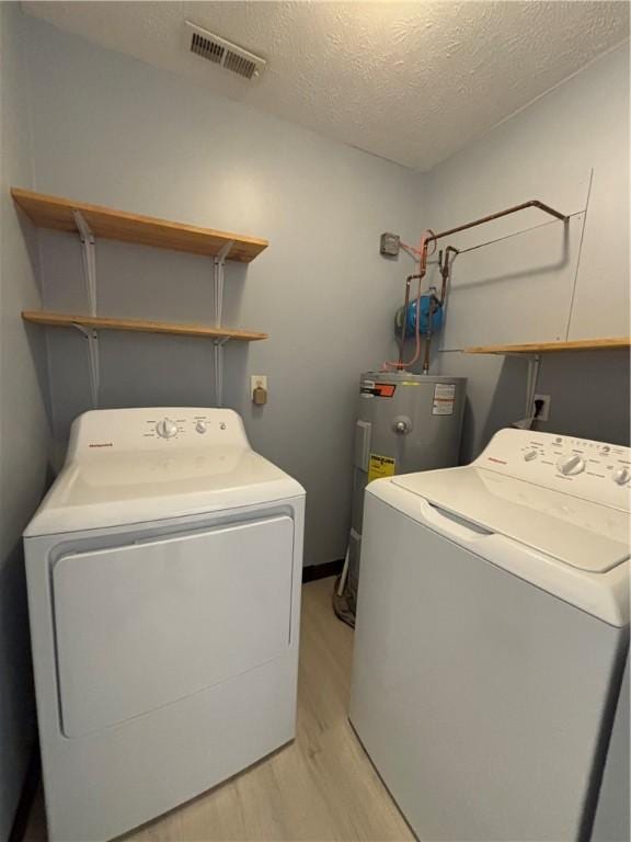 laundry room featuring separate washer and dryer, light hardwood / wood-style floors, water heater, and a textured ceiling