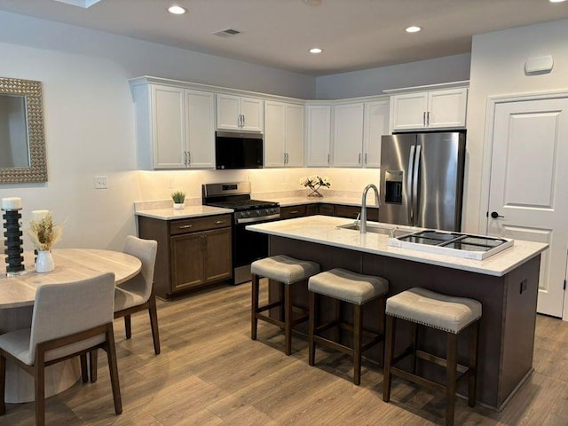 kitchen with appliances with stainless steel finishes, white cabinetry, sink, a breakfast bar area, and a kitchen island with sink