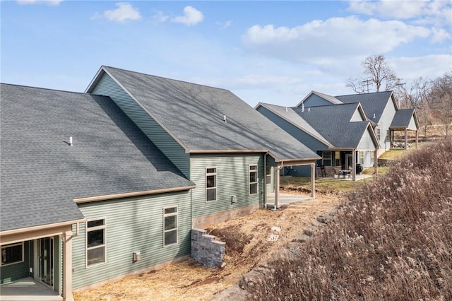 back of property with roof with shingles and a patio