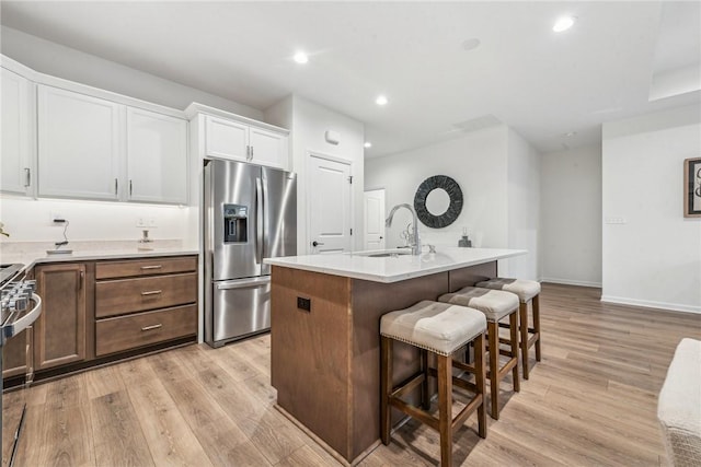 kitchen featuring a breakfast bar area, a kitchen island with sink, stainless steel appliances, a sink, and light wood-type flooring