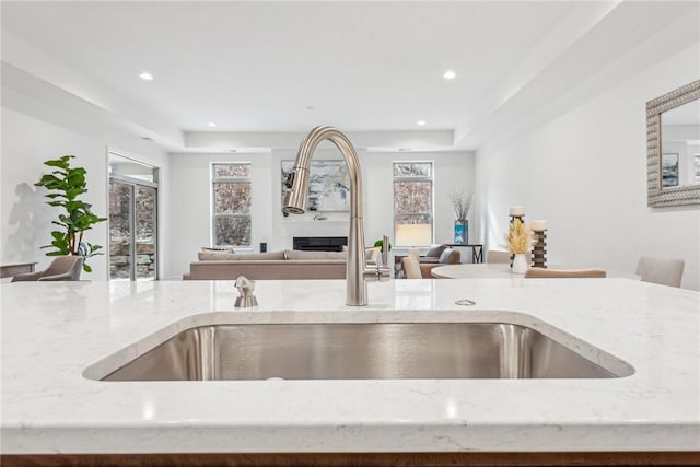 kitchen with light stone counters, a fireplace, recessed lighting, open floor plan, and a sink