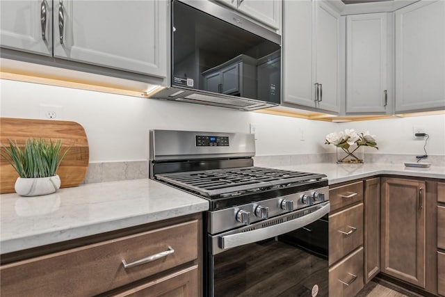 kitchen with stainless steel gas range oven, wood finished floors, and light stone countertops