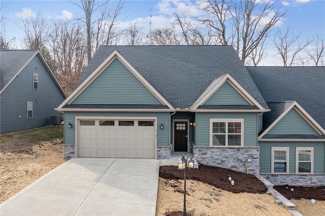 craftsman inspired home with roof with shingles, concrete driveway, central AC unit, a garage, and stone siding