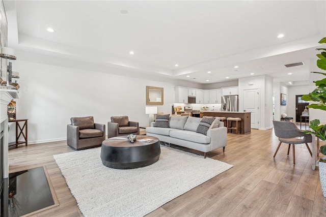 living room with a fireplace with flush hearth, light wood-type flooring, visible vents, and recessed lighting