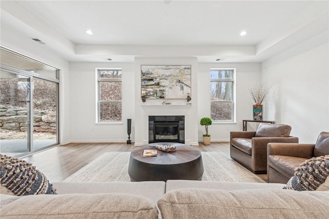 living area featuring a glass covered fireplace, wood finished floors, visible vents, and baseboards