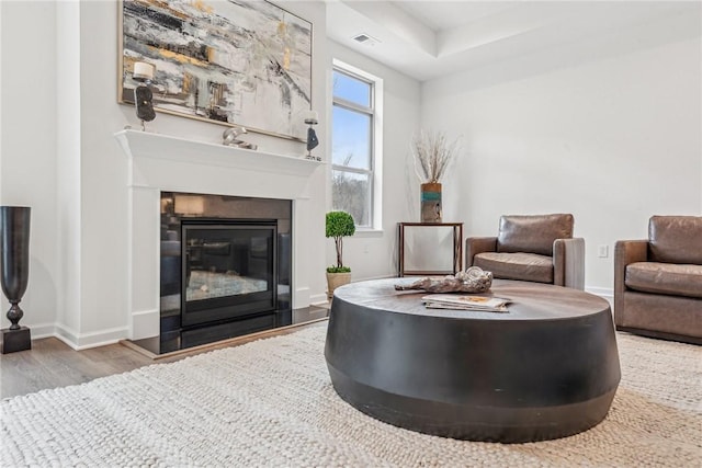 living area with baseboards, visible vents, wood finished floors, and a glass covered fireplace