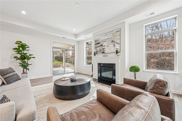 living room featuring baseboards, a fireplace with flush hearth, visible vents, and wood finished floors