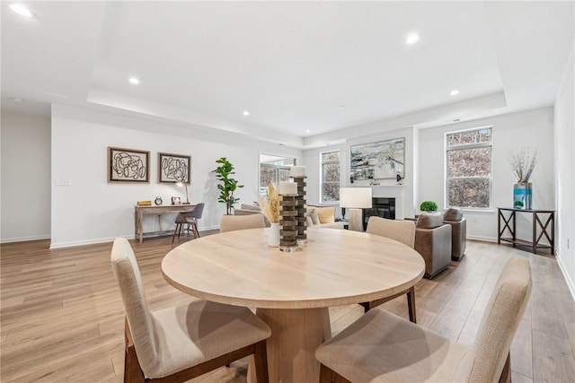 dining area with a glass covered fireplace, a raised ceiling, light wood-style flooring, and baseboards