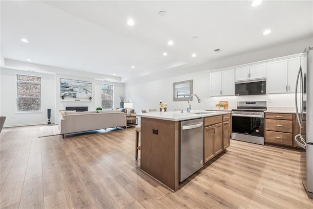 kitchen featuring open floor plan, appliances with stainless steel finishes, light wood-type flooring, and a center island with sink