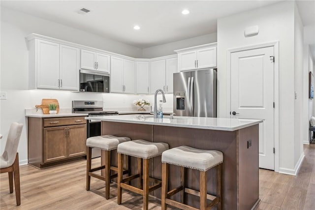 kitchen with stainless steel appliances, a kitchen bar, a sink, and light wood-style floors