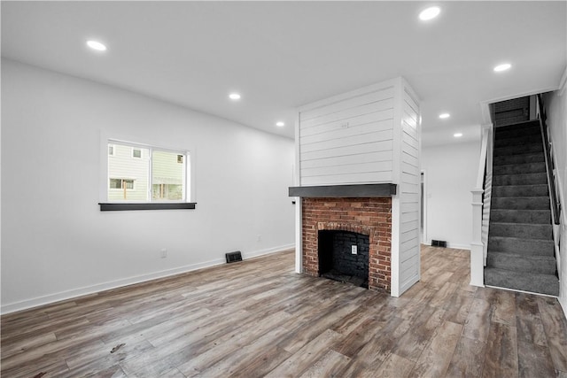 unfurnished living room featuring hardwood / wood-style floors and a brick fireplace