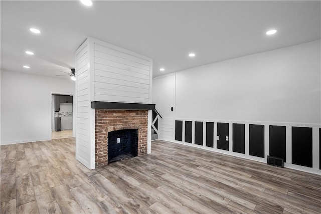 unfurnished living room with wood-type flooring, a brick fireplace, and ceiling fan