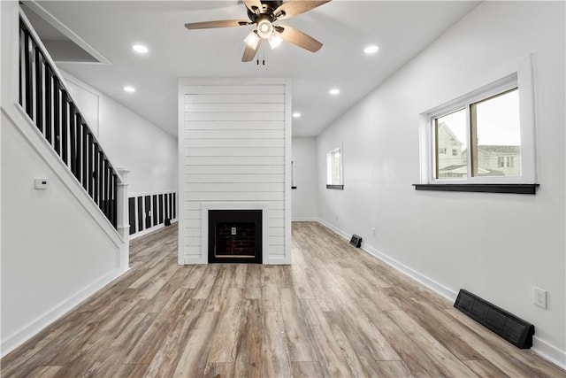 unfurnished living room featuring a large fireplace, ceiling fan, and light wood-type flooring