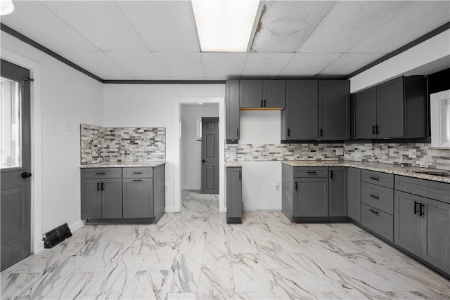 kitchen with tasteful backsplash, gray cabinets, light stone counters, and a drop ceiling