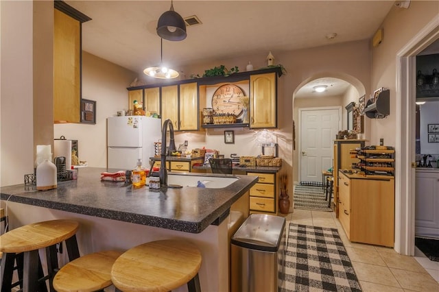 kitchen with sink, a breakfast bar area, light tile patterned flooring, kitchen peninsula, and white fridge