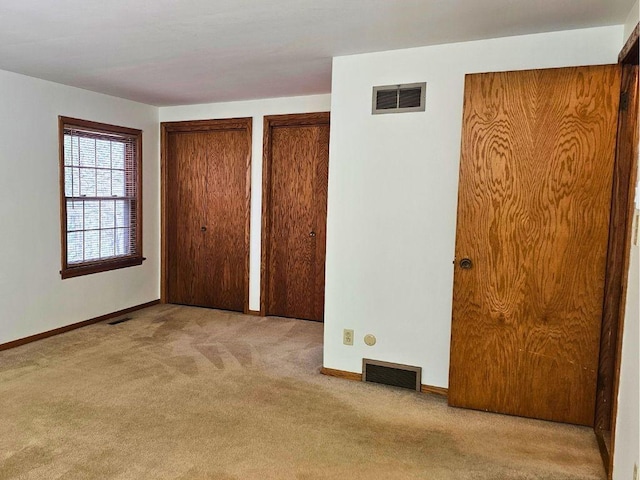 unfurnished bedroom featuring light colored carpet and multiple closets