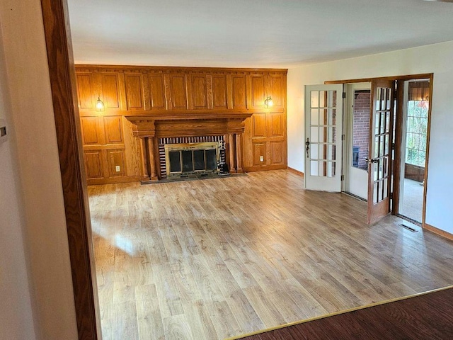 unfurnished living room featuring a brick fireplace, light hardwood / wood-style floors, and french doors