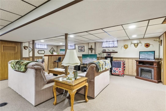 living room with a drop ceiling, light colored carpet, and wood walls