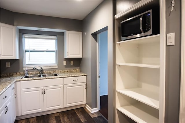 kitchen featuring white cabinetry, dark wood-type flooring, light stone countertops, and sink