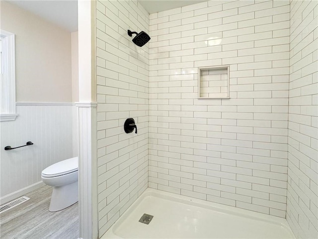 bathroom with wood-type flooring, tiled shower, and toilet