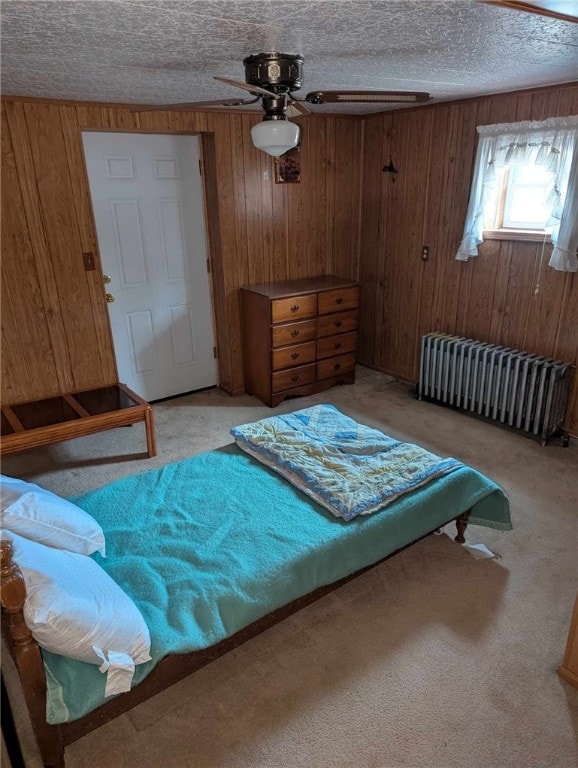 bedroom with radiator, light colored carpet, a textured ceiling, and wood walls