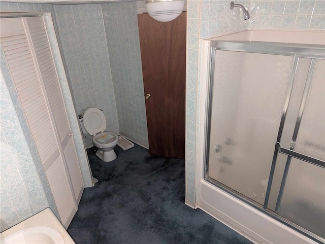 bathroom featuring tile walls, toilet, and combined bath / shower with glass door