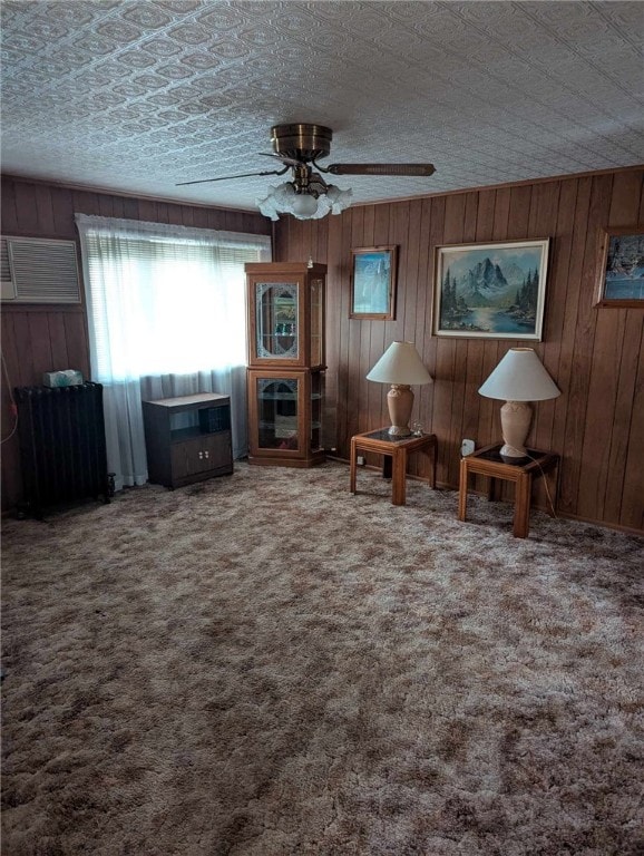 carpeted living room with a textured ceiling, ceiling fan, and wood walls