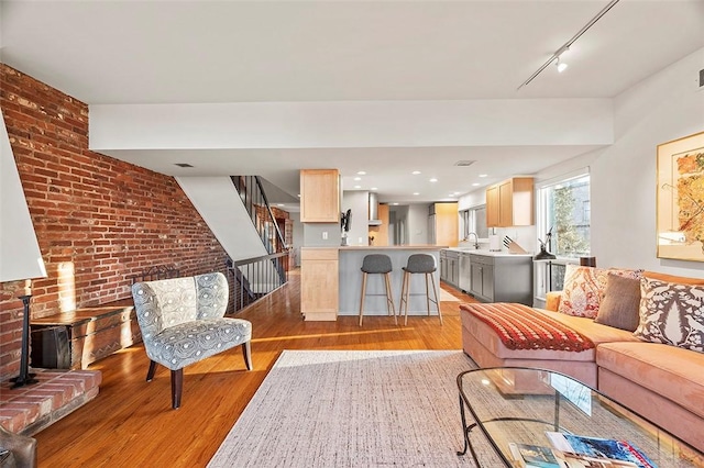 living room with rail lighting, brick wall, sink, and light hardwood / wood-style floors